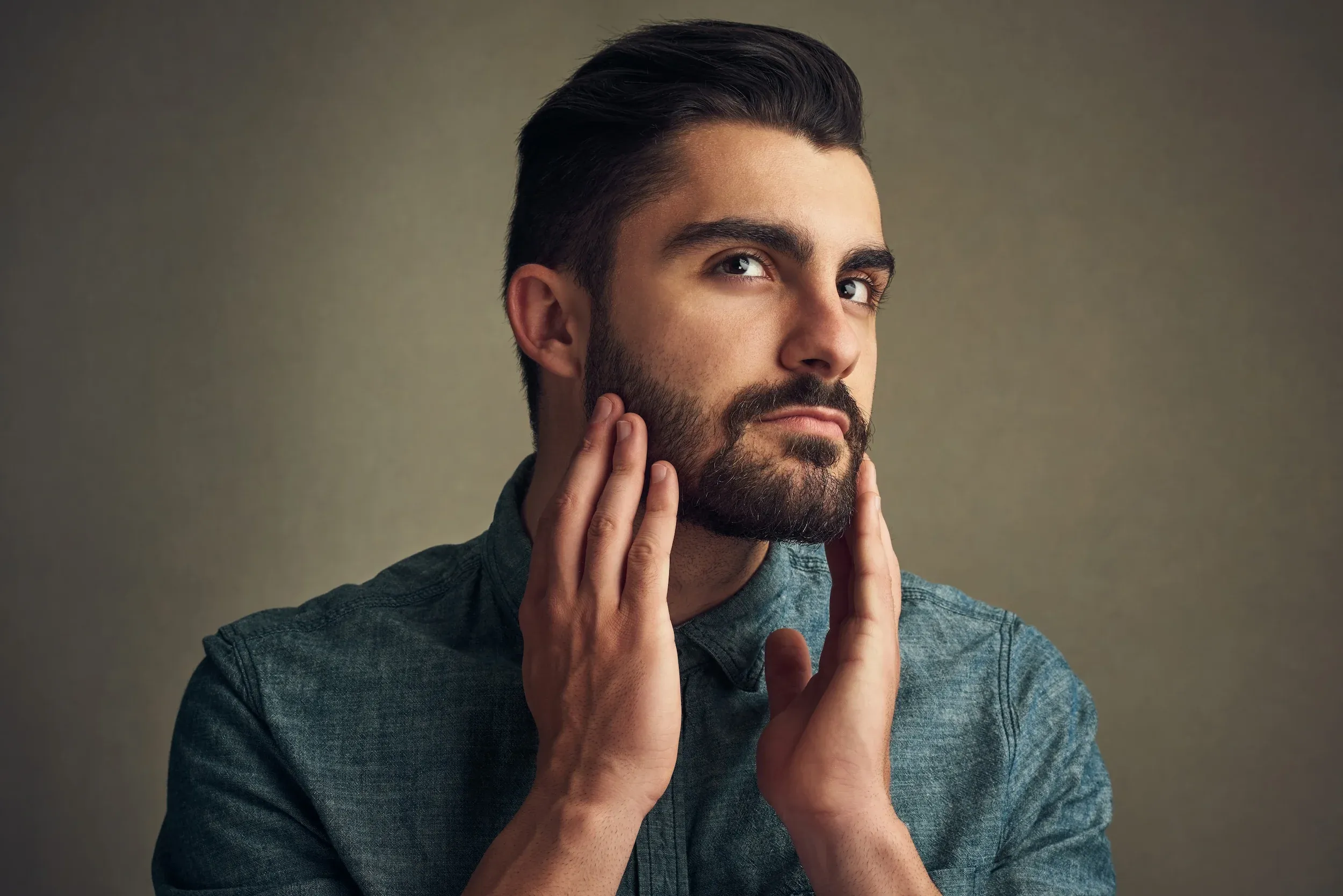 Man touching his jawline and styled hair with contemplative expression - male hair loss concerns at ANU Face Mind Body