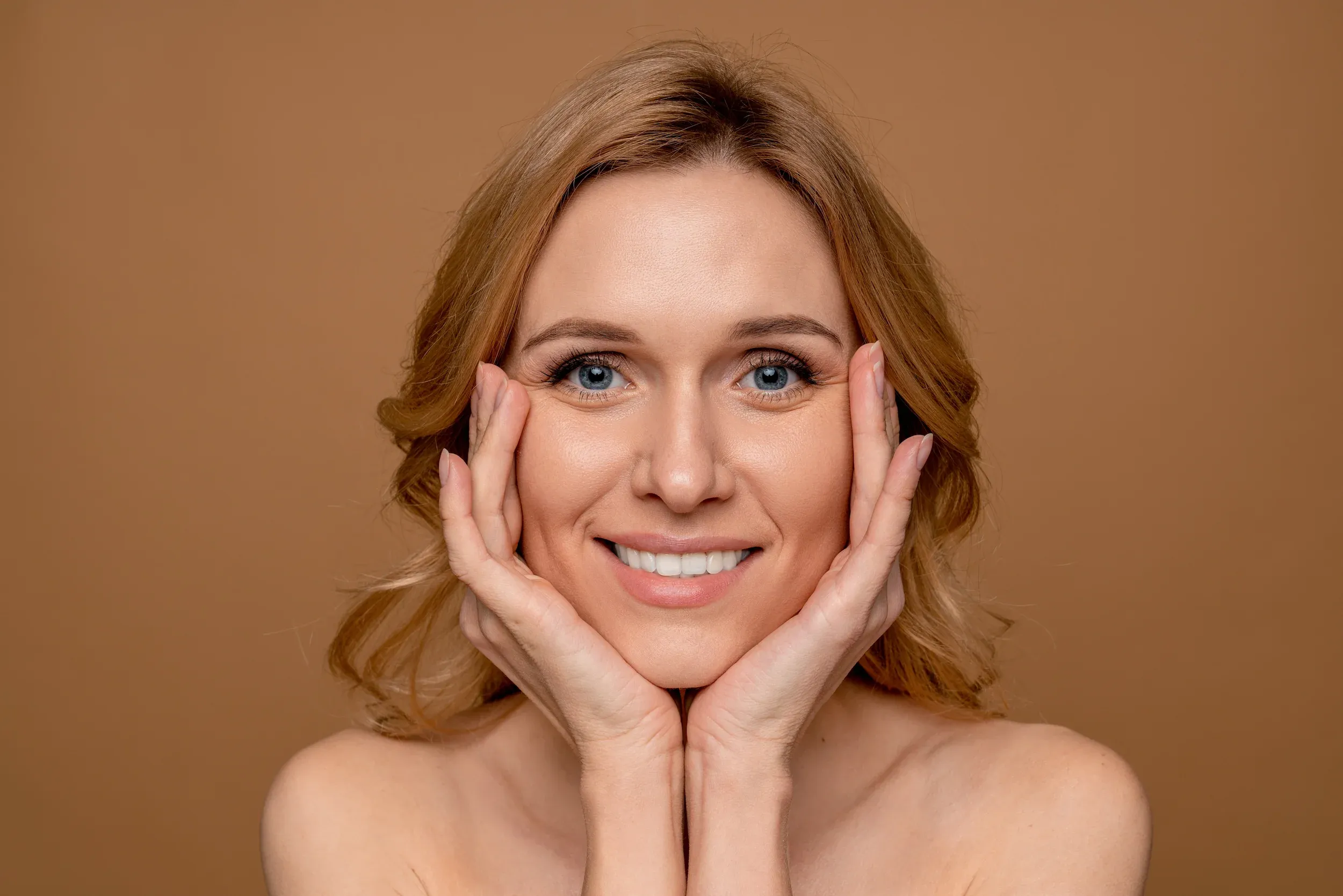 Woman with smooth glowing complexion gently touching her face - anti-aging skincare consultation at ANU Face Mind Body