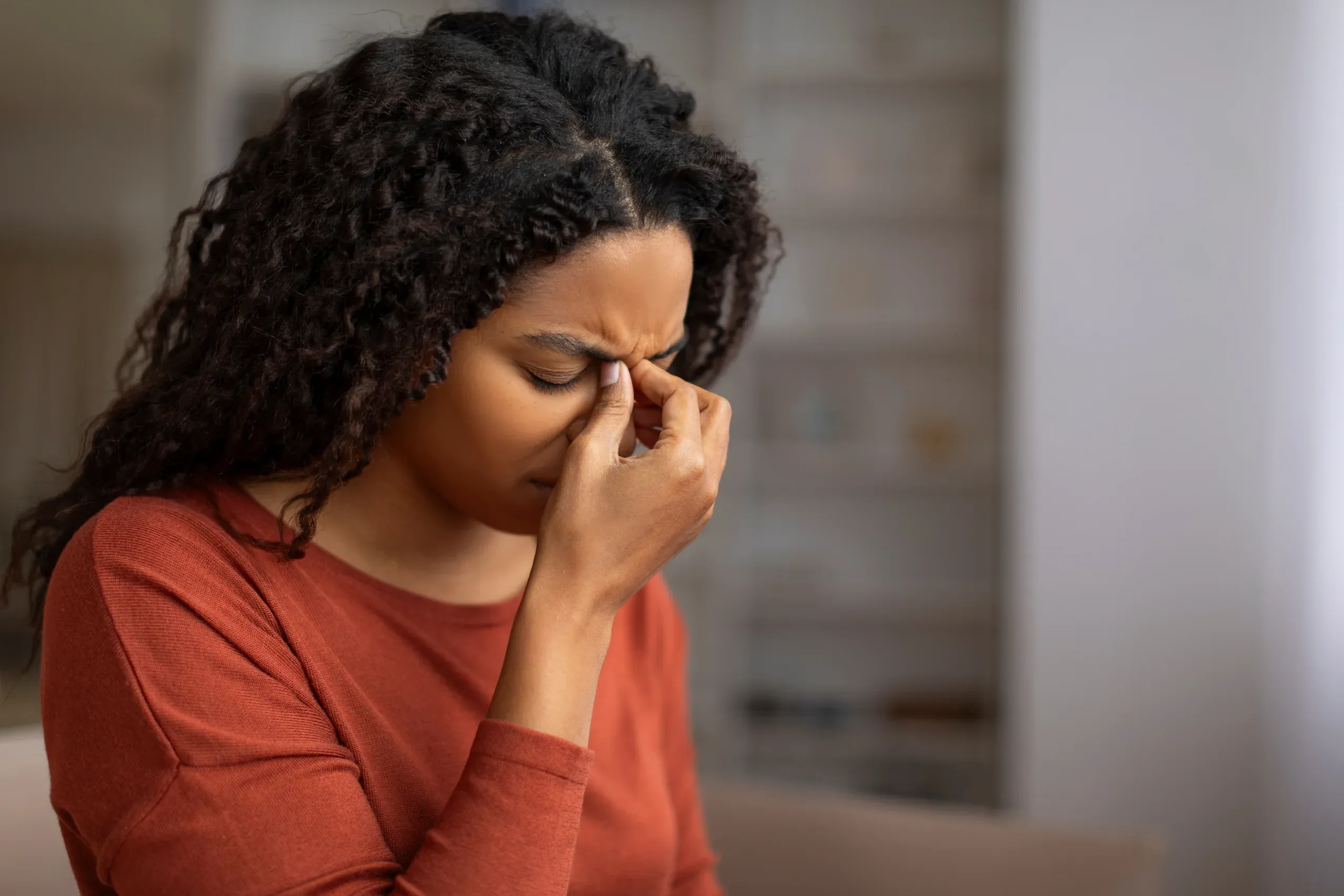 Woman pinching bridge of nose with eyes closed showing tension and mental distress - mental health support at ANU Face Mind Body
