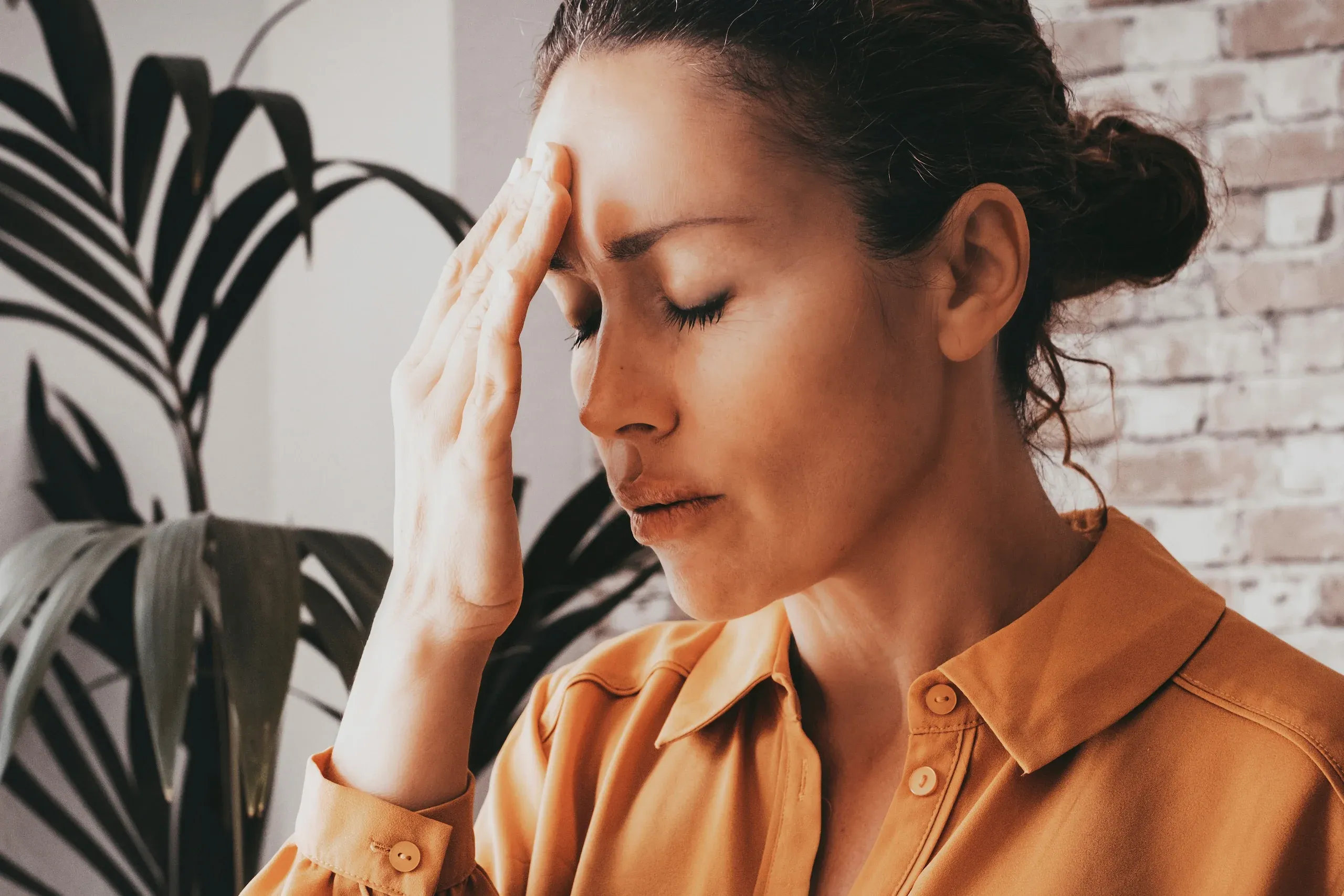 Woman pressing hand to forehead with eyes closed experiencing stress - understanding causes of anxiety and depression