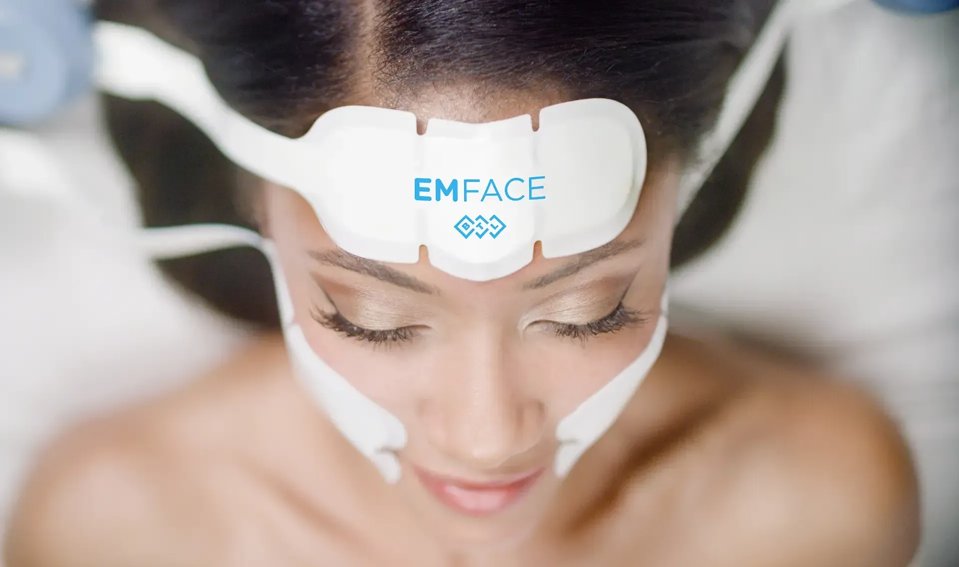 Soft brand-blue gradient background representing Emface facial rejuvenation