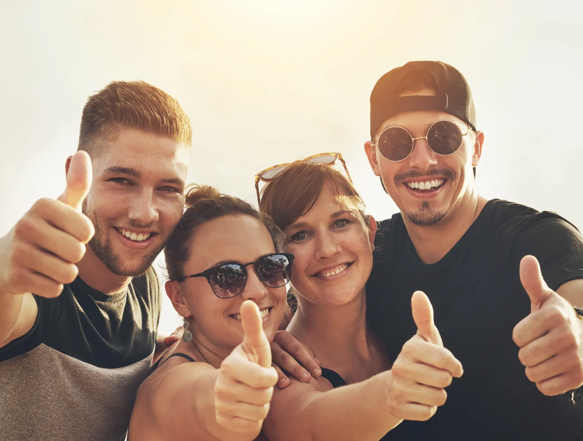 Group of happy young people giving thumbs up outdoors in the sunshine