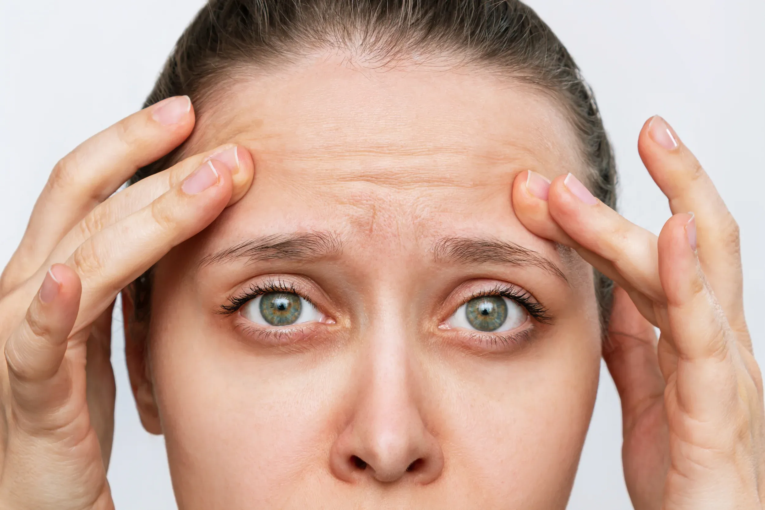 Woman examining forehead lines and frown lines in mirror at Heritage Wellness & Med Spa Crescent Springs